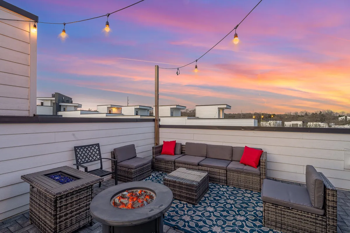 An inviting rooftop setting with a cozy fire pit, abundant outdoor seating, twinkling string lights, and a sunset sky, this image offers a glimpse of memorable evenings spent together outdoors. The mood is warm and welcoming, encouraging togetherness and relaxation for groups of all ages.