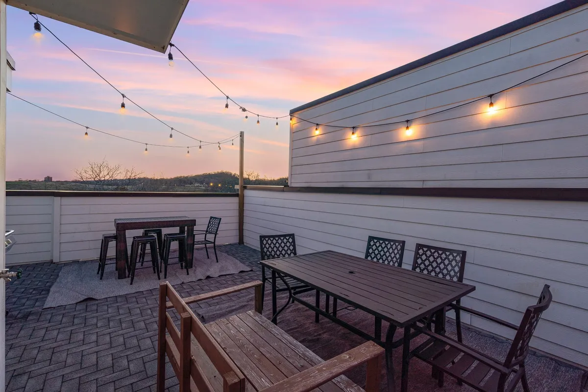 An inviting rooftop patio scene with string lights, cozy patio furniture, and a sunset sky. The atmosphere is intimate and relaxed, perfect for unwinding after a day of urban exploration and enjoying panoramic city views in the evening.