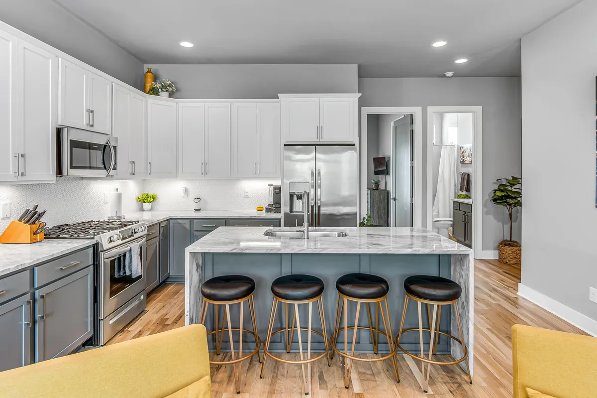 A modern kitchen with a sleek marble island and seating, stainless steel appliances, and open shelving. The layout is ideal for entertaining, cooking, or enjoying casual meals together. The warm, welcoming mood is accentuated by thoughtful lighting and contemporary finishes.