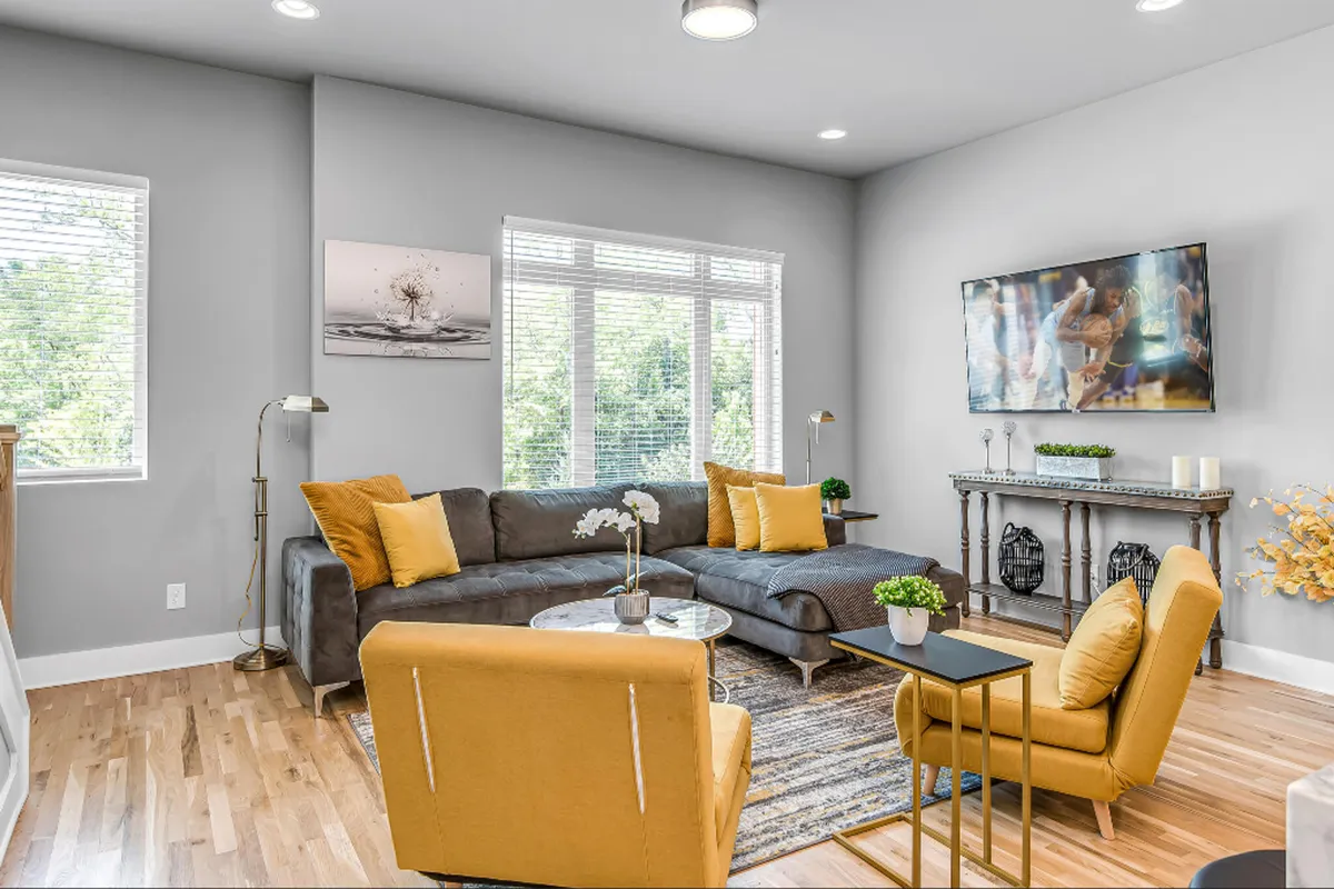 A cozy, cheerful living room with a sofa, yellow chairs, a coffee table, and a TV mounted on the wall. Decorative wall art and warm lighting create an inviting space for relaxing, socializing, or movie nights with loved ones.