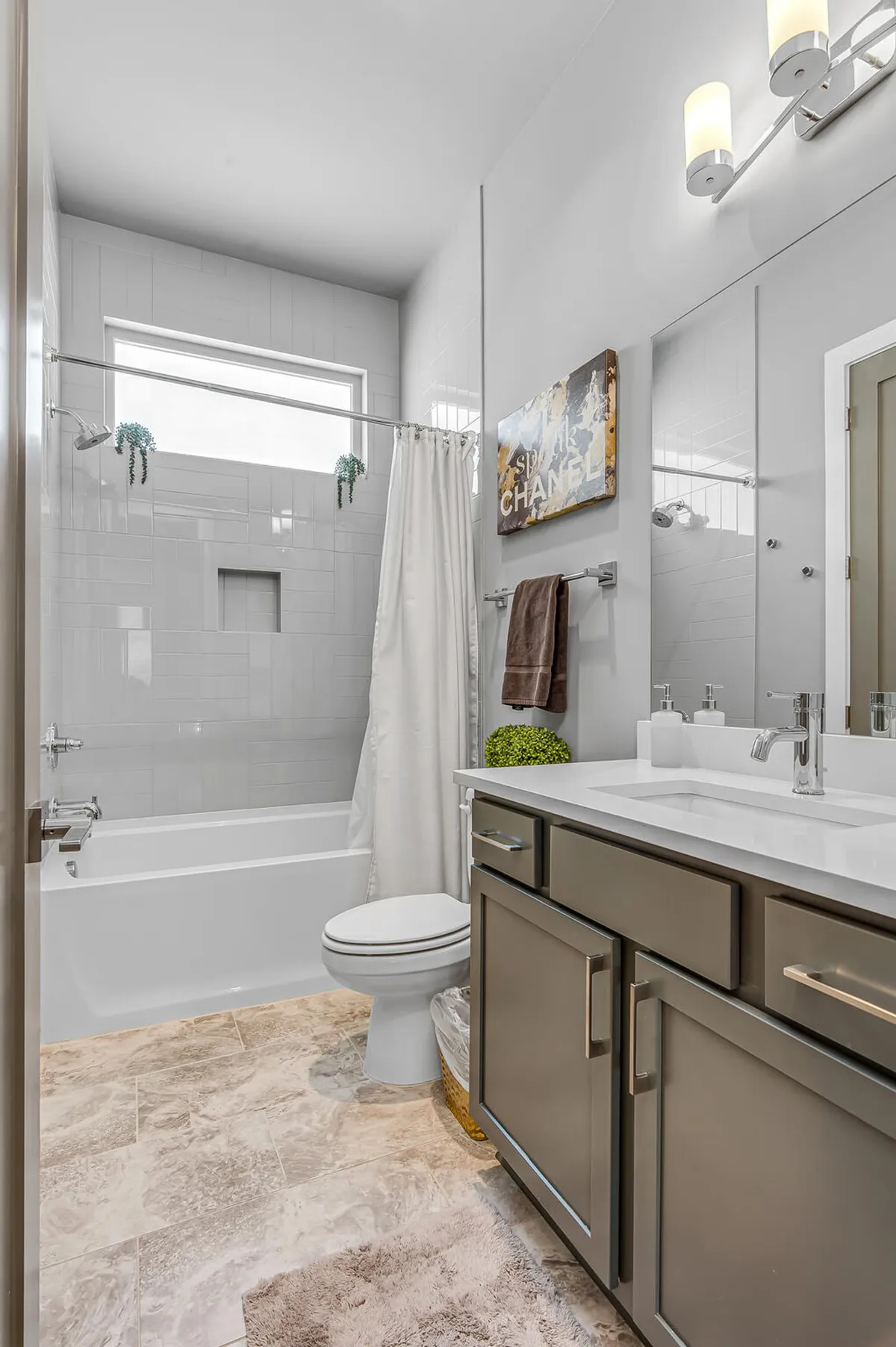 A gleaming bathroom featuring a modern bathtub, sleek vanity with ample counter space, a mirror, elegant wall art, and a neatly arranged towel rack. The space feels calm and spa-like, inviting guests to relax and indulge in self-care routines.